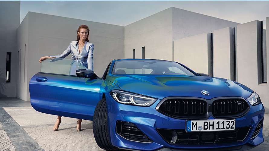 The BMW M850i xDrive Coupé G15 LCI Facelift 2022 M Portimao Blue metallic front view standing with female model in open front door