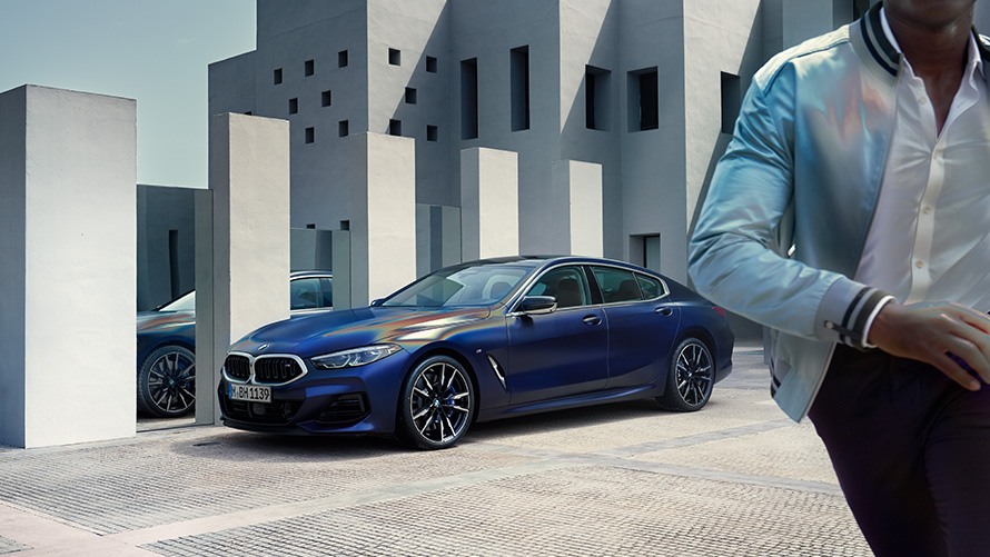 منظر أمامي ثلاثي الزوايا للسيارة BMW M850i xDrive Gran Coupé G16 LCI Facelift 2022 باللون الأزرق تنزانايت فروزين المعدني ضمن برنامج BMW Individual مع شاب عارض في المقدمة