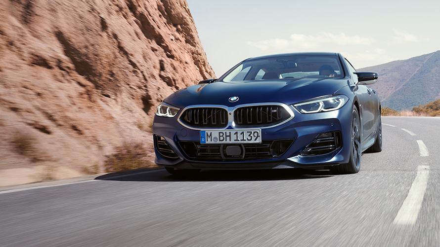 منظر أمامي ثلاثي الزوايا للسيارة BMW 8 Series Gran Coupé M850i xDrive 2022 G16 LCI Facelift باللون الأزرق تنزانيت فروزين المعدني ضمن برنامج BMW Individual أثناء القيادة